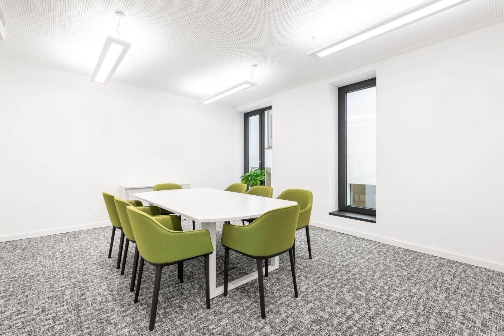 Heller Besprechungsraum mit Teppichboden, einem weißen Tisch und grünen Stühlen, ideal für kleine Teams.