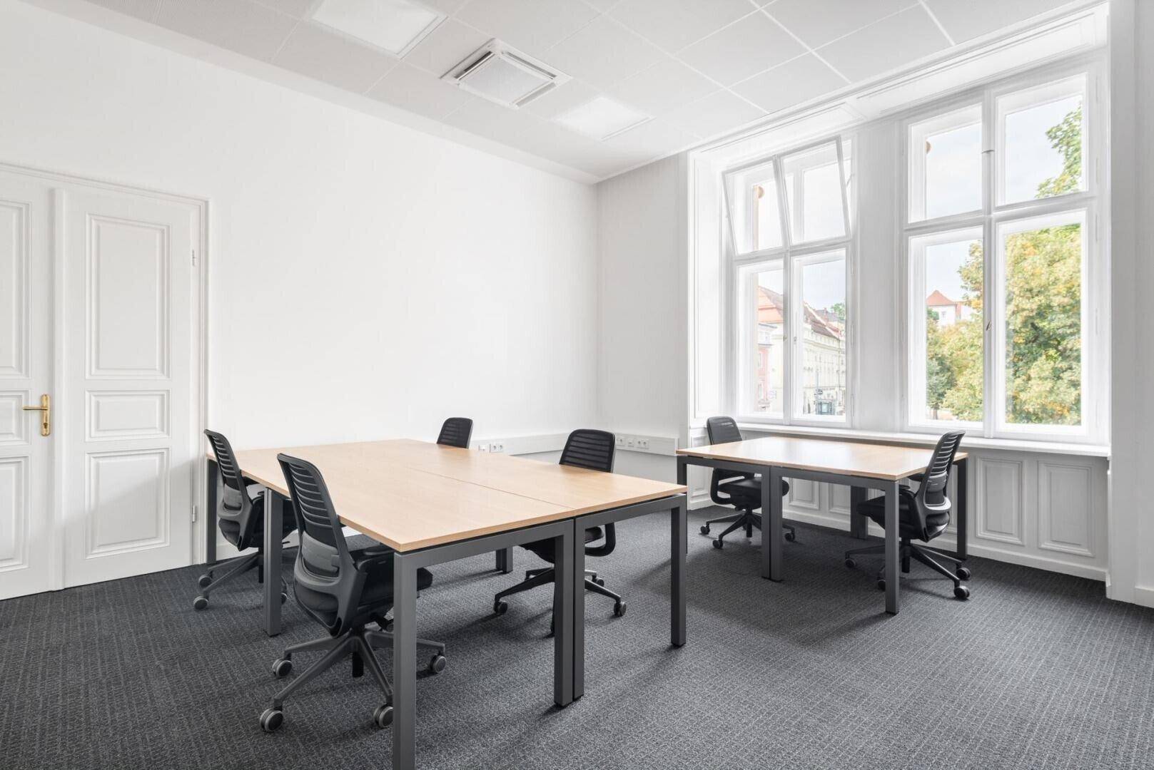 Helles Büro mit Teppichboden, zwei Schreibtischen und großen Fenstern, die eine angenehme Arbeitsatmosphäre schaffen.