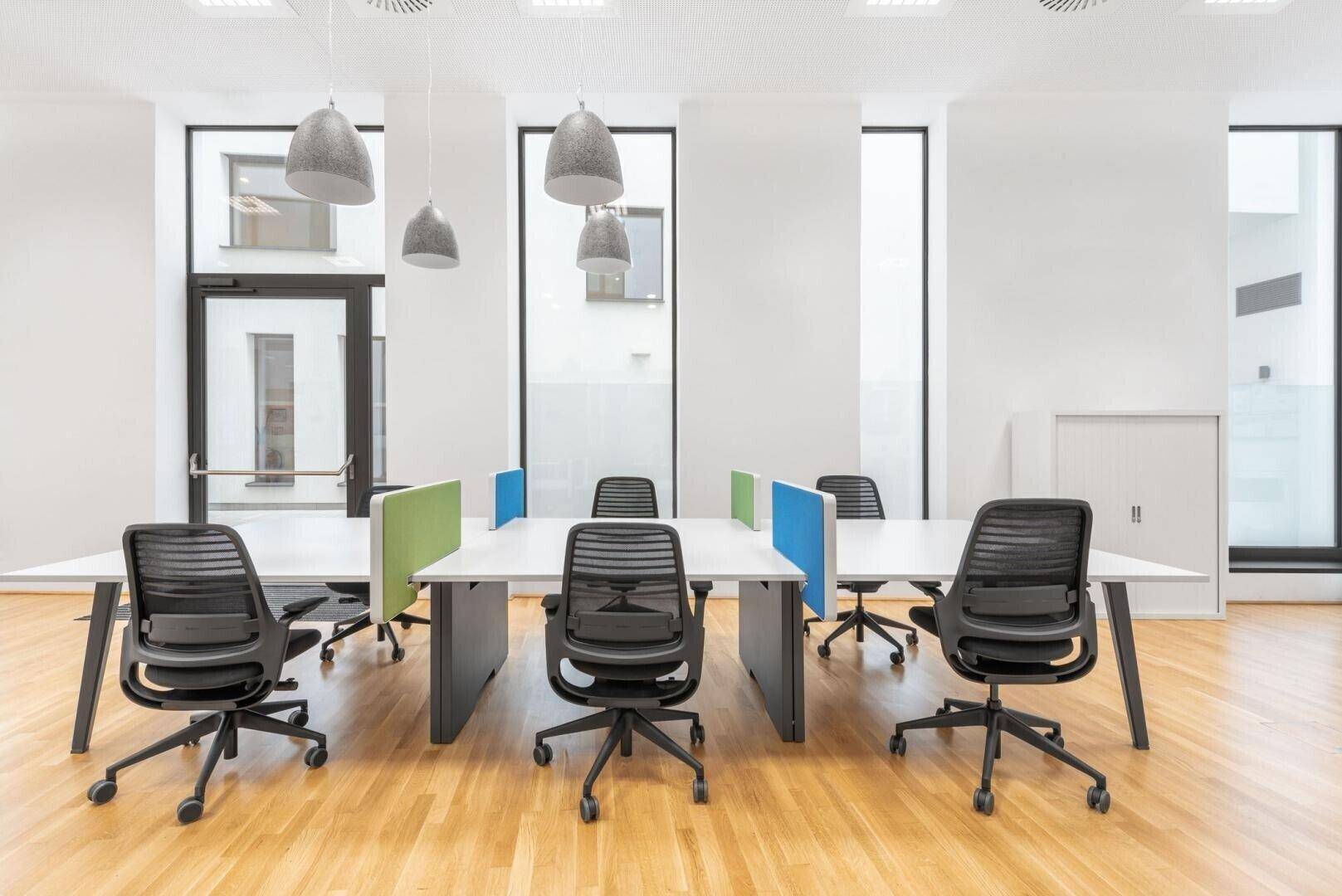 Offener Bürobereich mit mehreren Arbeitsplätzen, ergonomischen Stühlen und großen Fenstern für viel Licht.