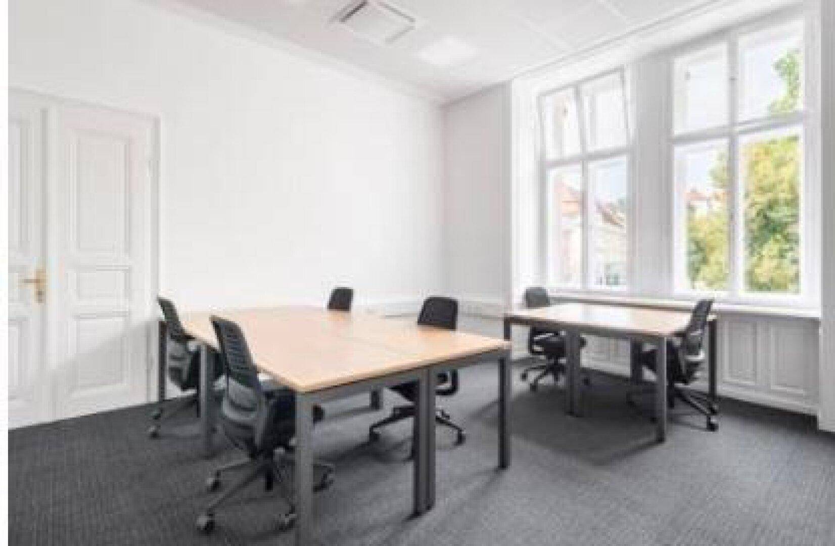 Klassisches Büro mit hohen Fenstern, Teppichboden und mehreren Schreibtischen in einem Altbau.