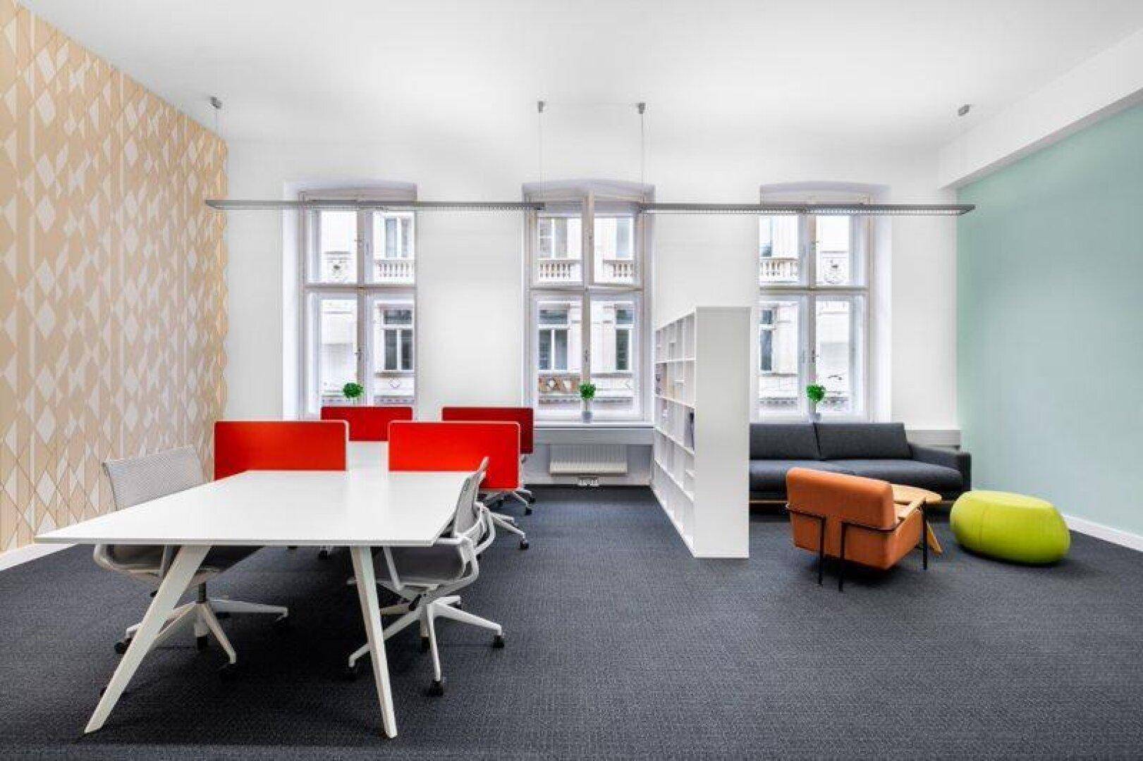 Großes offenes Büro mit mehreren Arbeitsplätzen, einem Loungebereich und hohen Fenstern.