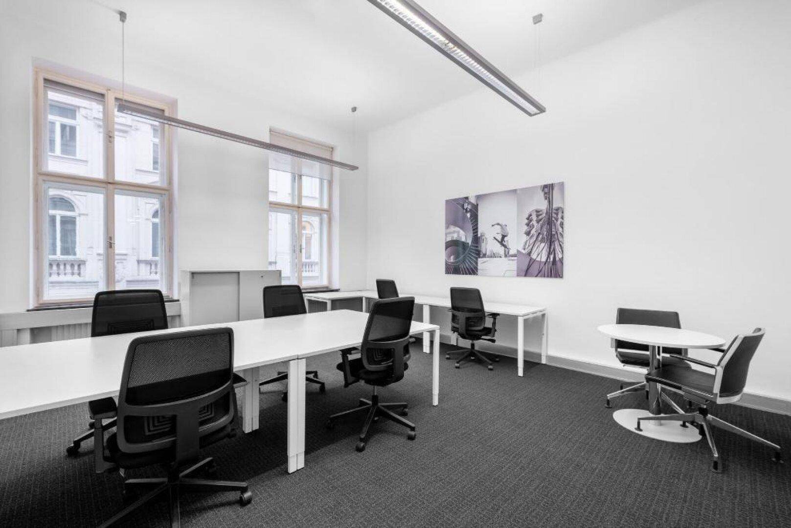 Helles und geräumiges Büro mit mehreren Arbeitsplätzen, modernen Büromöbeln und großen Fenstern.