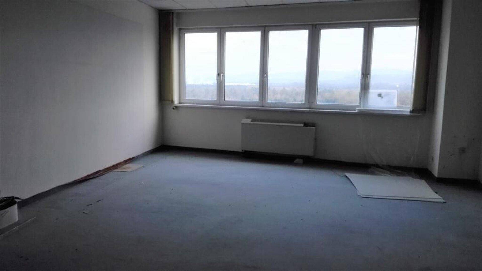 Helles, leeres Büro mit großen Fenstern und einem Heizkörper, bereit für die Einrichtung.