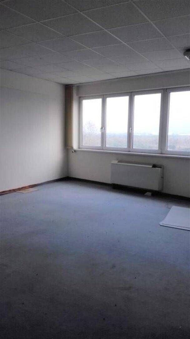 Leeres Büro mit großen Fenstern, die viel Tageslicht hereinlassen, und einem Heizkörper.