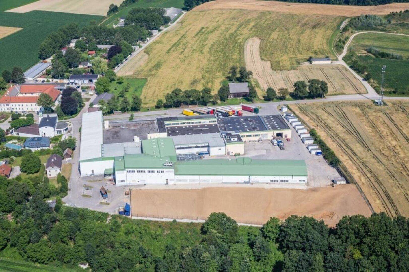 Luftaufnahme eines großen Industrie- und Logistikkomplexes, umgeben von Feldern und ländlicher Landschaft.