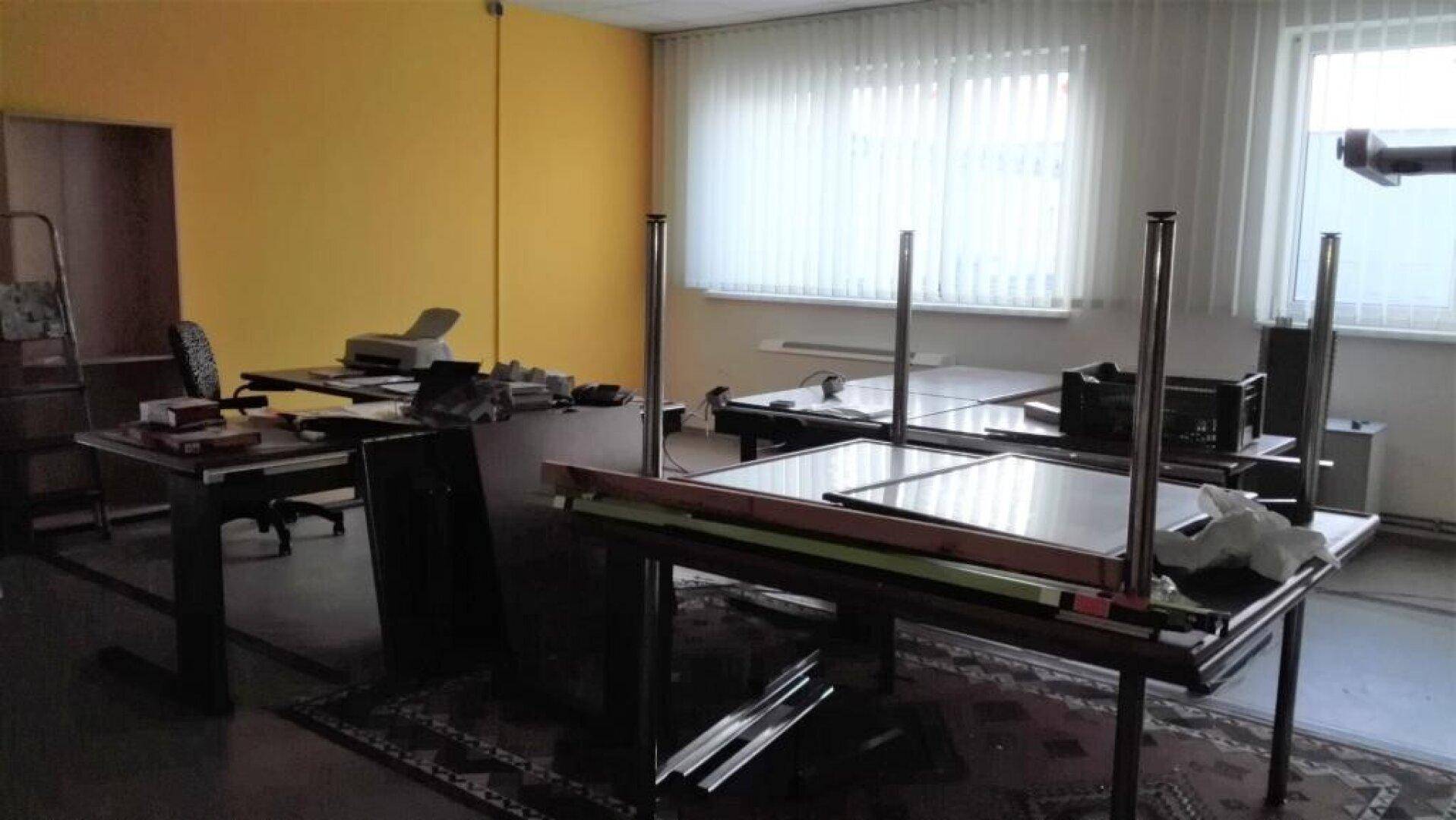 Büro mit gelb gestrichenen Wänden, mehreren Tischen und einem Teppichboden.
