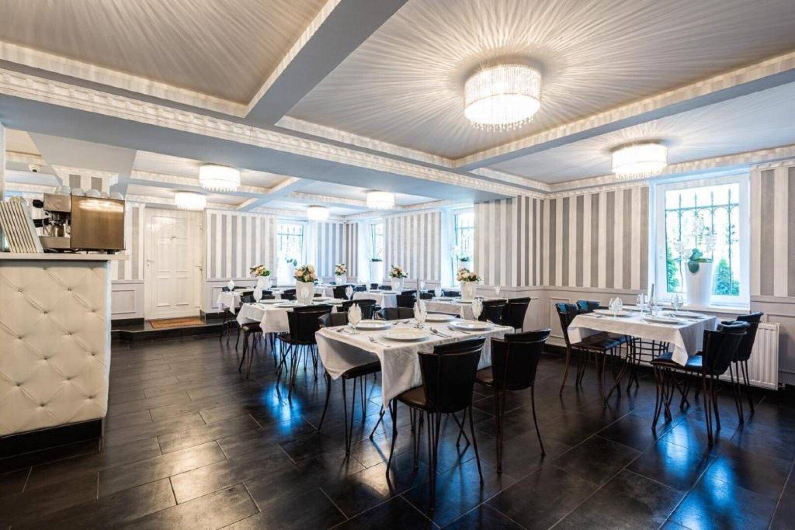 Heller Speisesaal mit vielen Fenstern, dunklem Fliesenboden und eleganten Kronleuchtern.