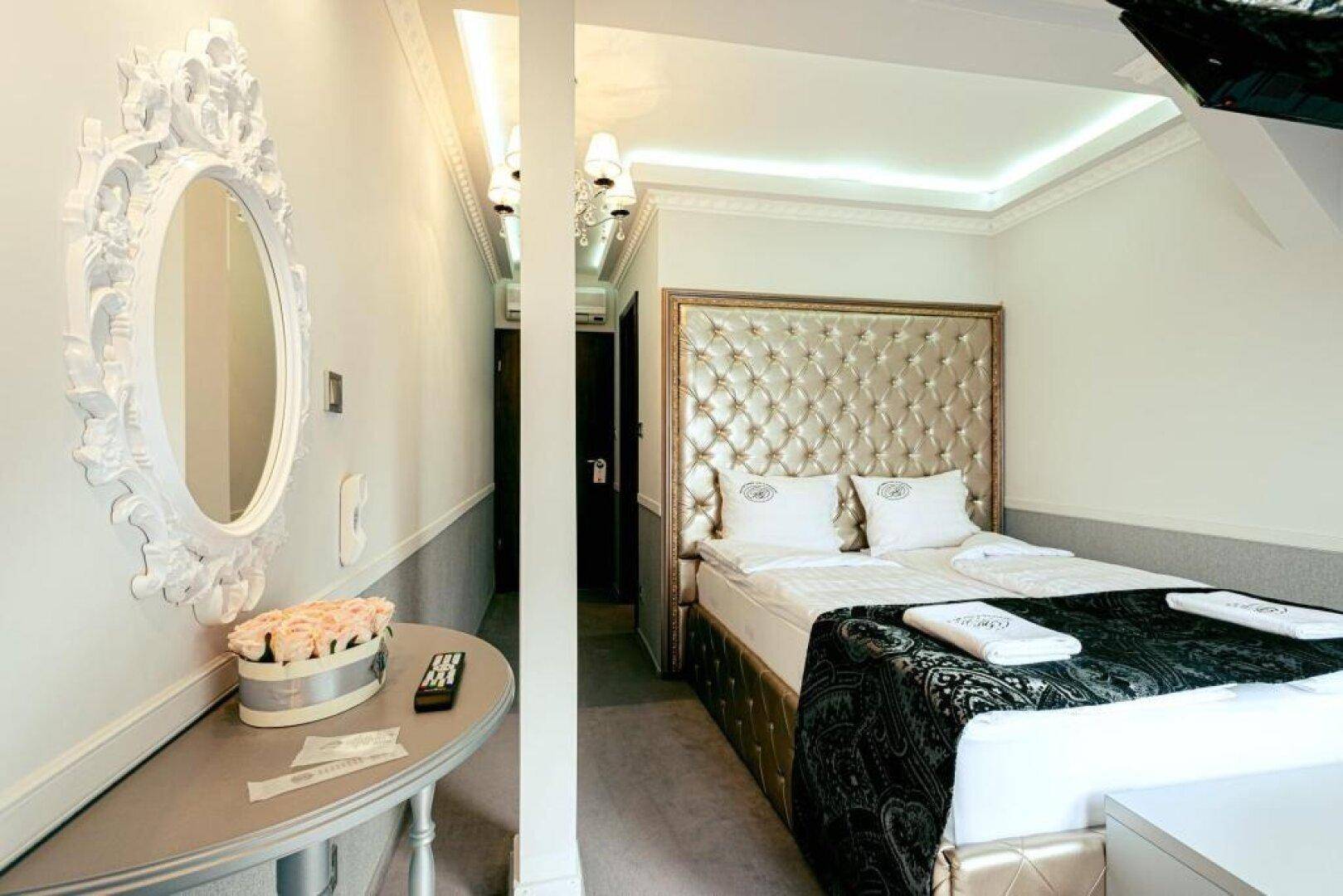 Helles Schlafzimmer mit einem gepolsterten Bett, einem dekorativen Spiegel und einem schmalen Flur.