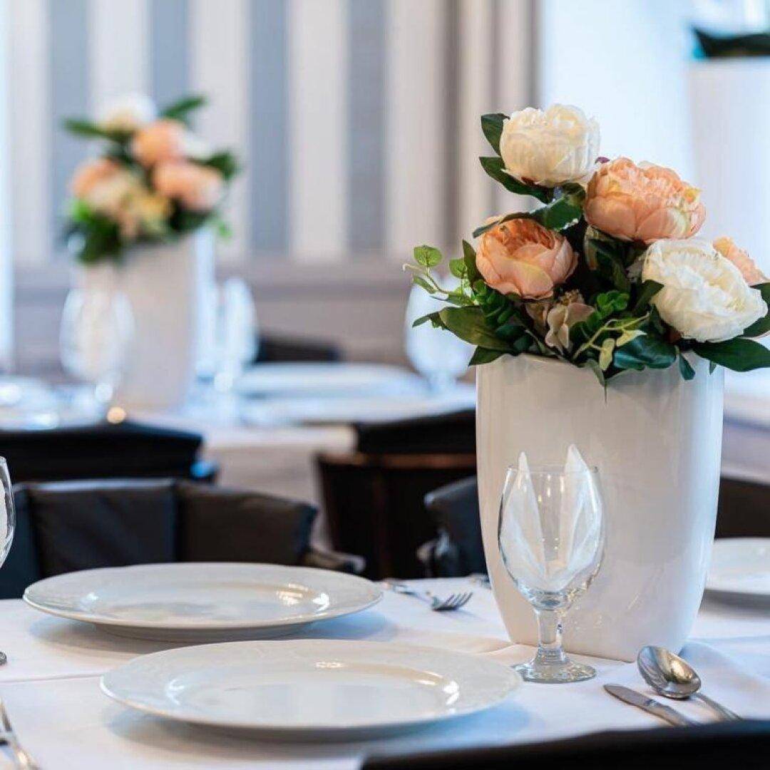 Nahaufnahme eines elegant gedeckten Tisches mit frischen Blumen und weißem Geschirr in einem Restaurant.
