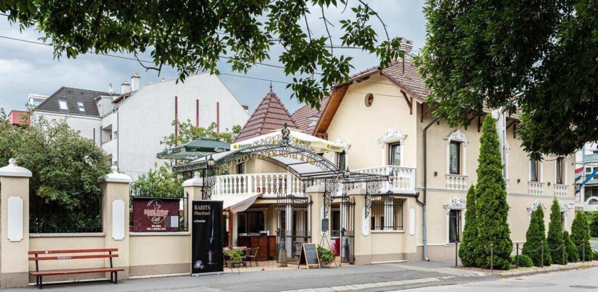 Ansicht des Gebäudes von der Straße mit einer einladenden Terrasse und gepflegten Nadelbäumen.