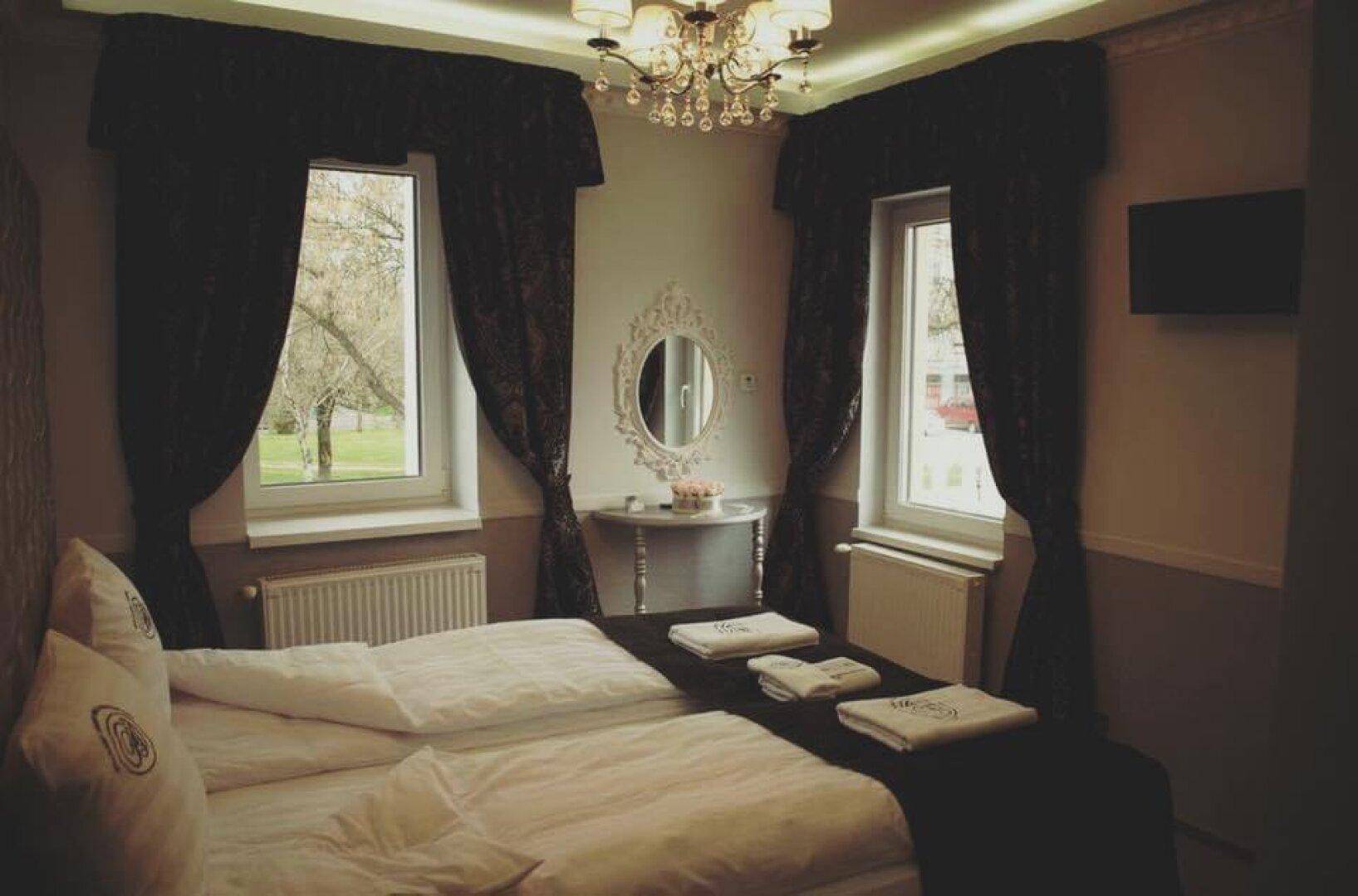 Gemütliches Schlafzimmer mit zwei Einzelbetten, dunklen Vorhängen und einem Fenster mit Blick ins Grüne.