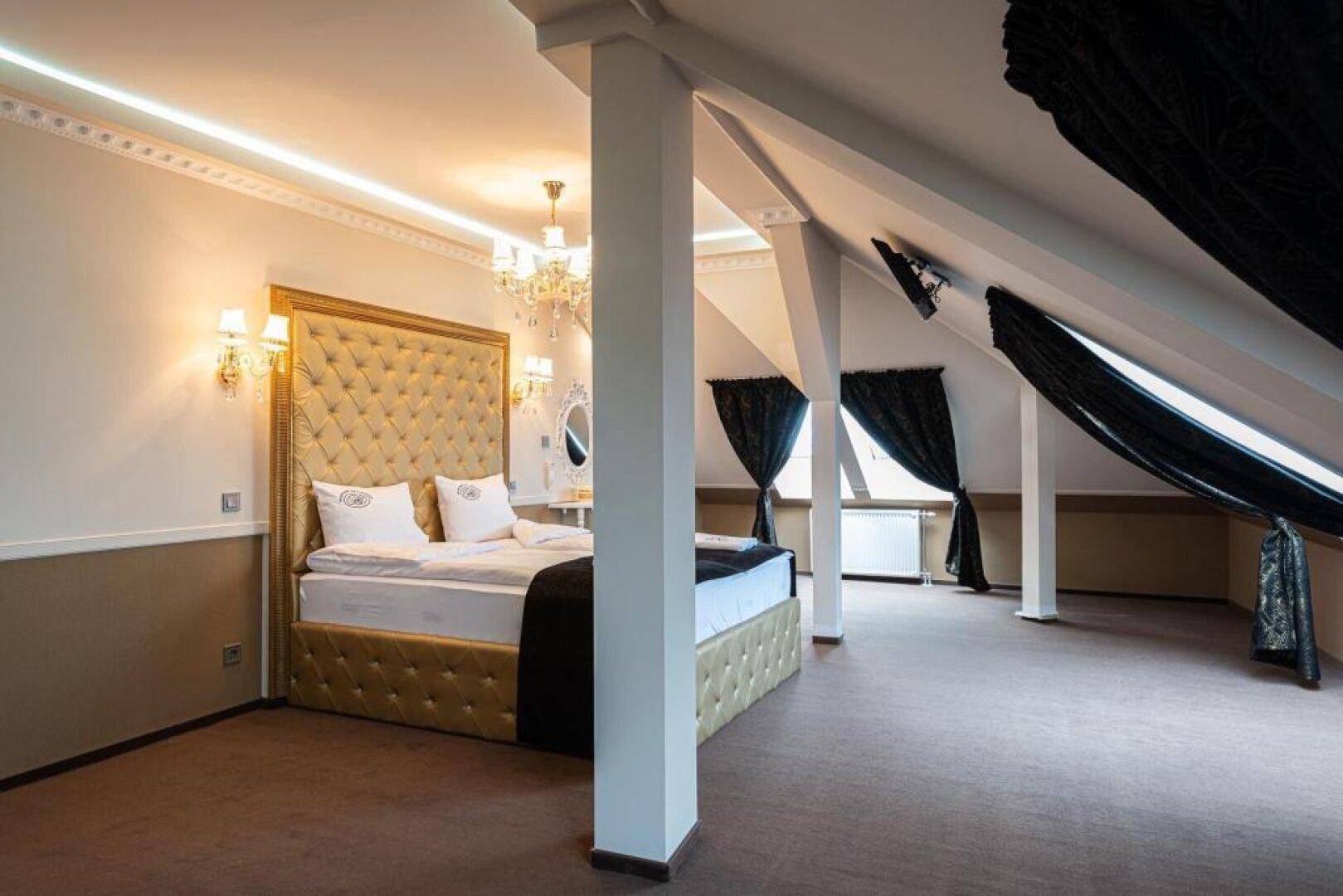 Großes Schlafzimmer im Dachgeschoss mit schrägen Wänden, einem luxuriösen Bett und Säulen.