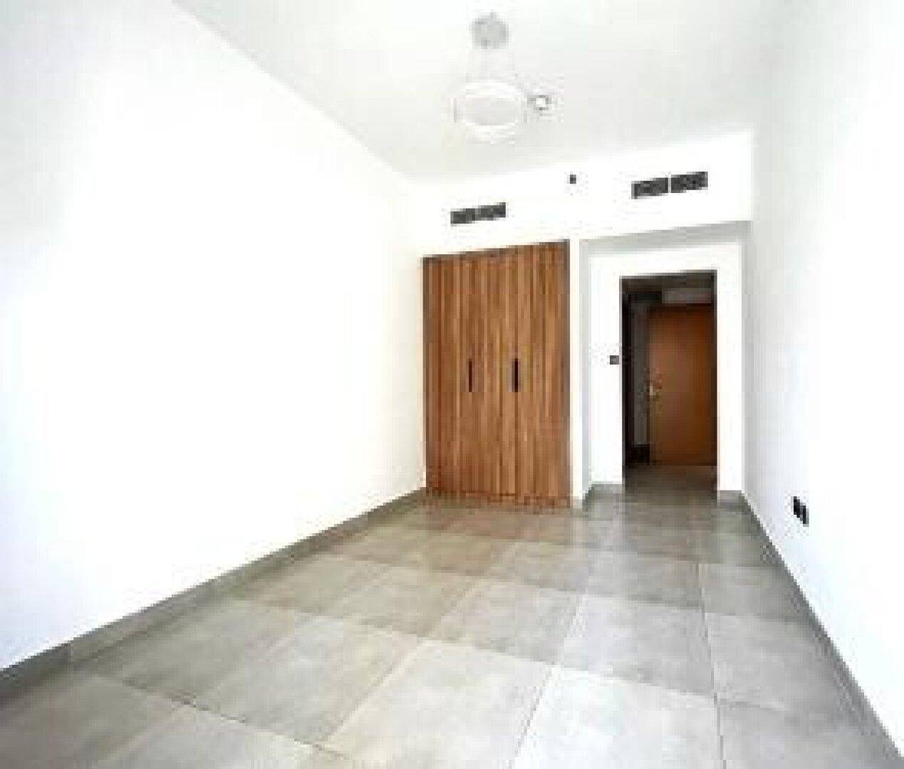 Leeres Schlafzimmer mit hellen Wänden, Fliesenboden und integriertem Holzschrank.