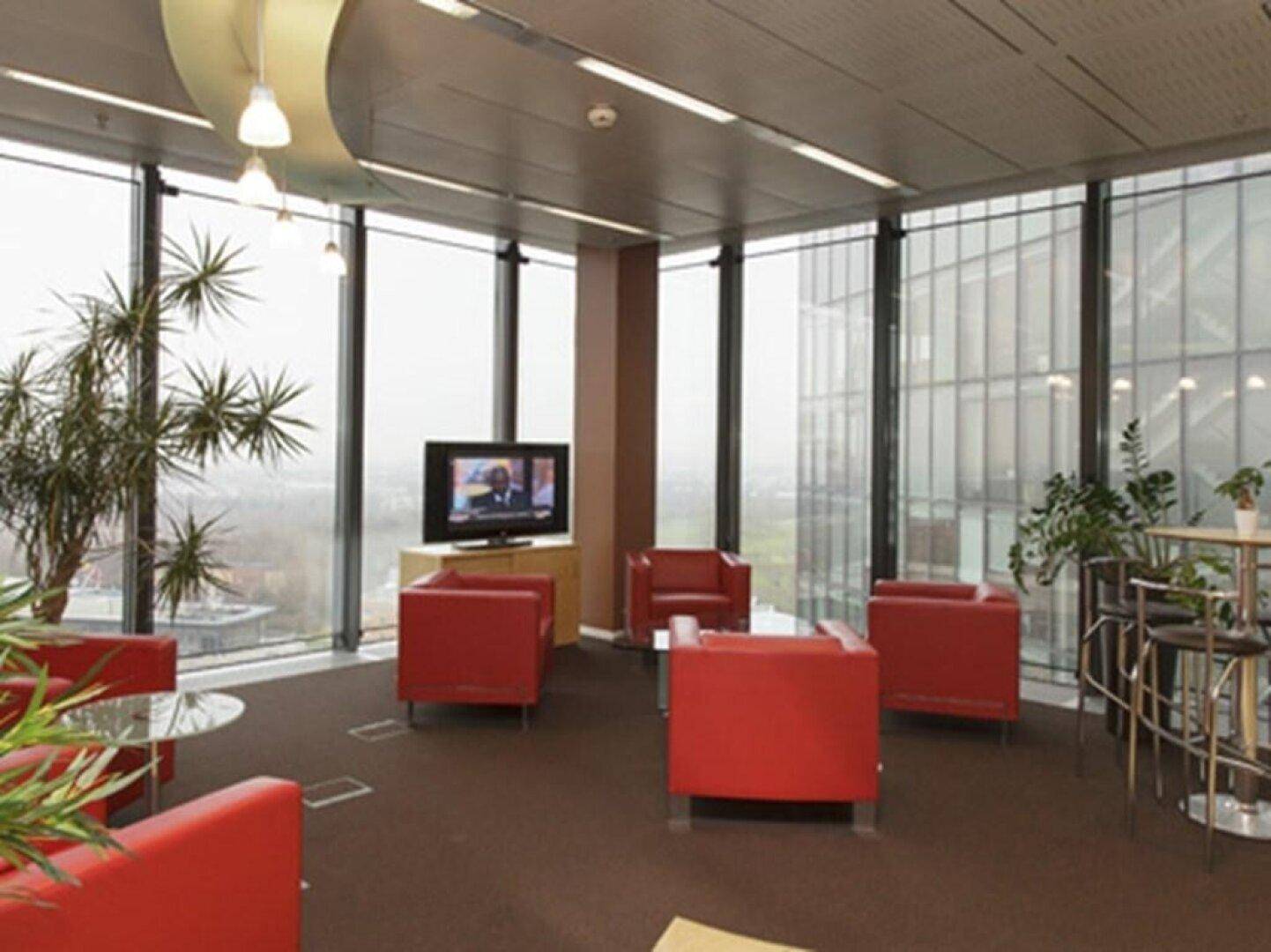 Geräumiger Loungebereich mit roten Sesseln, Fernseher und großen Fenstern mit Stadtblick.