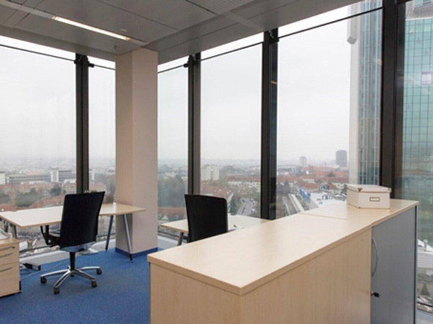 Offener Bürobereich mit mehreren Arbeitsplätzen, blauer Teppichboden und Panoramablick auf die Stadt.