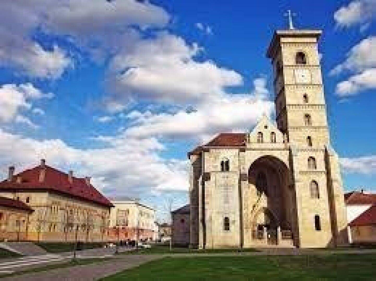 Eine beeindruckende historische Kirche mit einem hohen Uhrturm, umgeben von gepflegten Grünflächen unter strahlend blauem Himmel.
