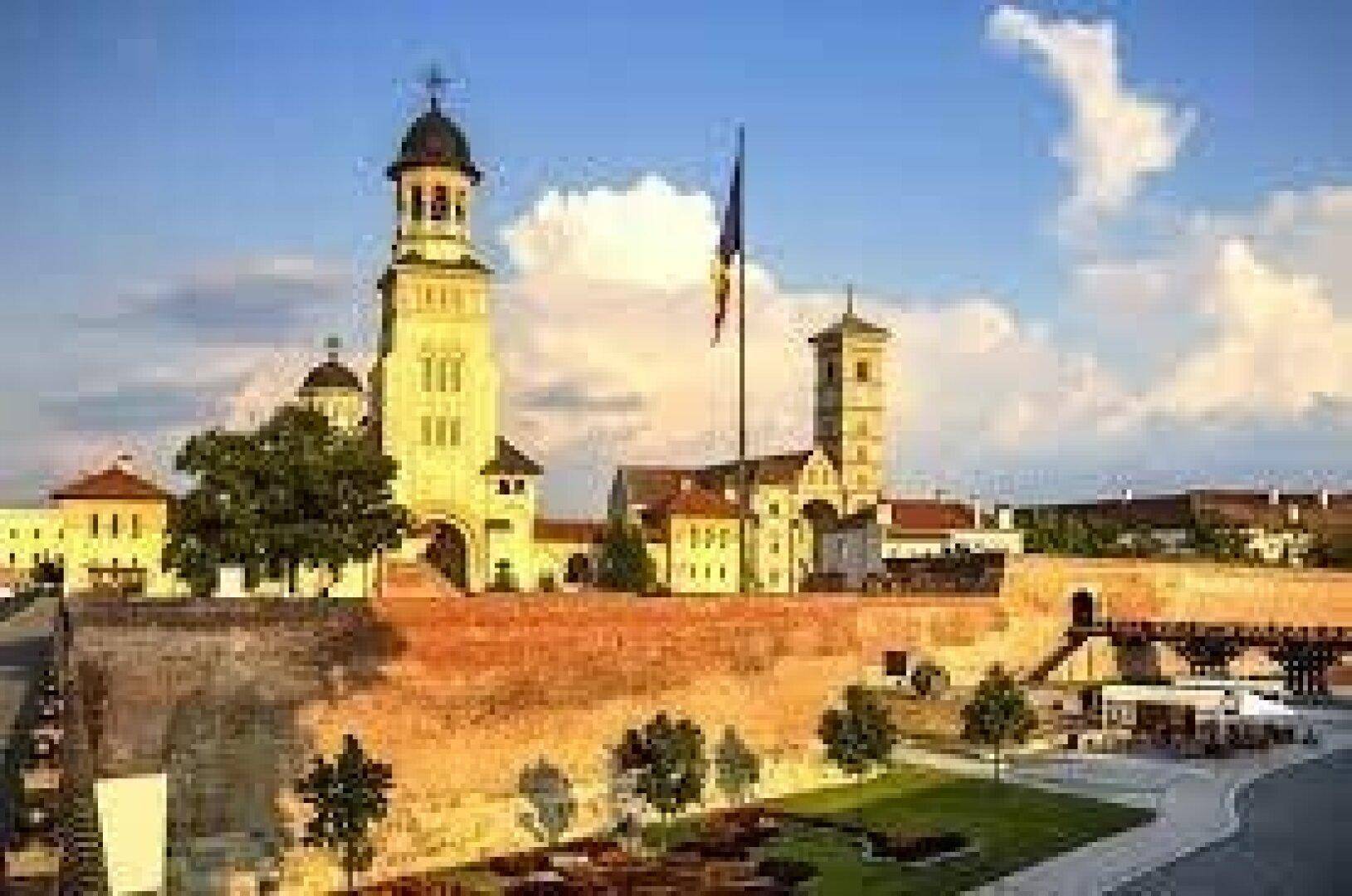 Panoramablick auf eine historische Festung mit imposanten Türmen, alten Mauern und grünen Anlagen unter blauem Himmel.
