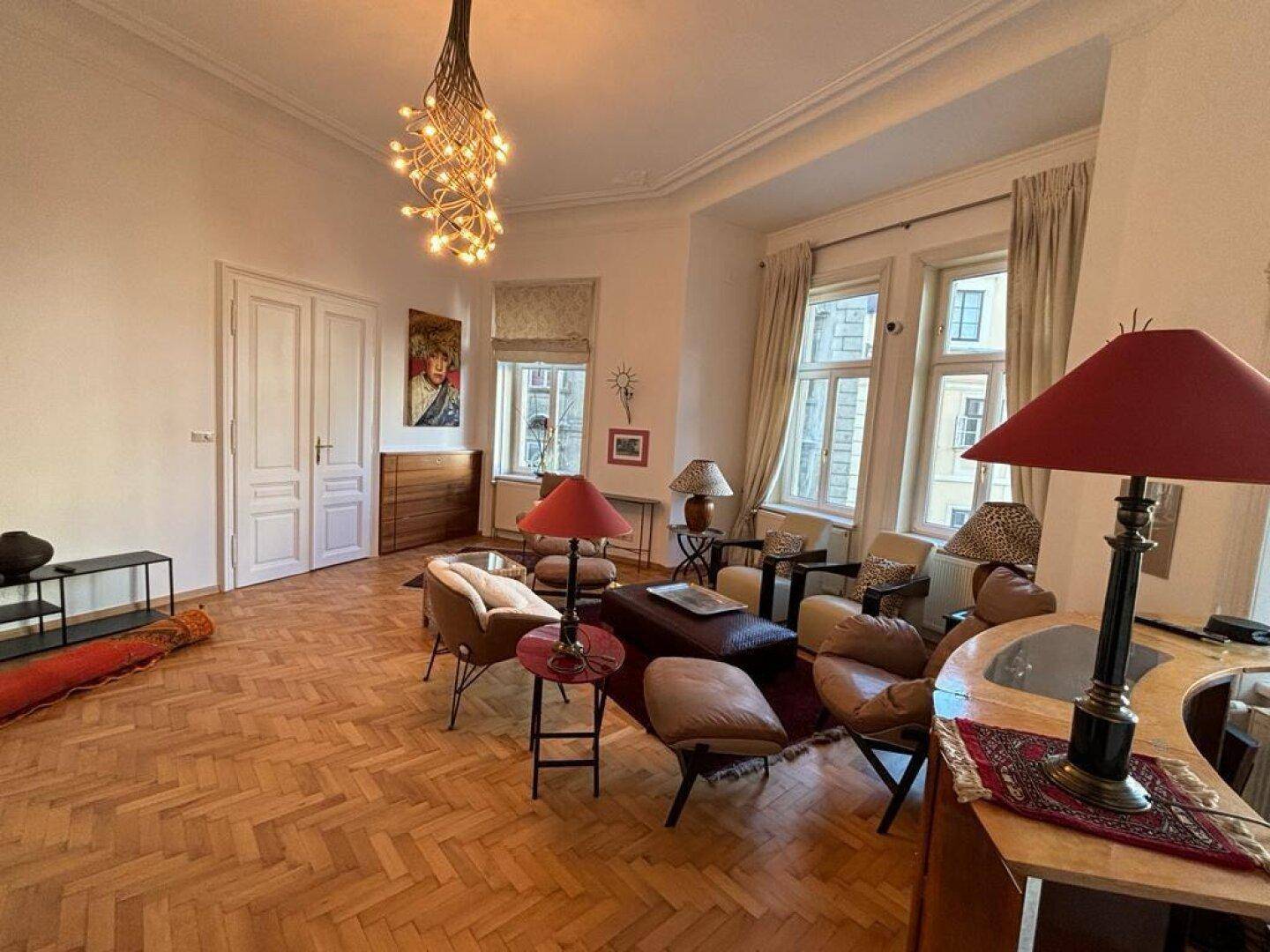Geräumiges Wohnzimmer mit elegantem Fischgrätparkett und großen Fenstern.