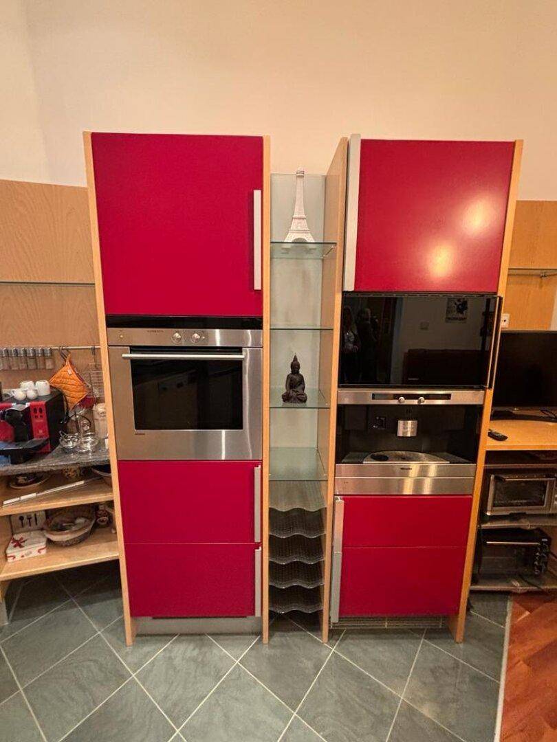Integrierte Küchengeräte mit Backofen und Kaffeemaschine in roten Hochschränken.