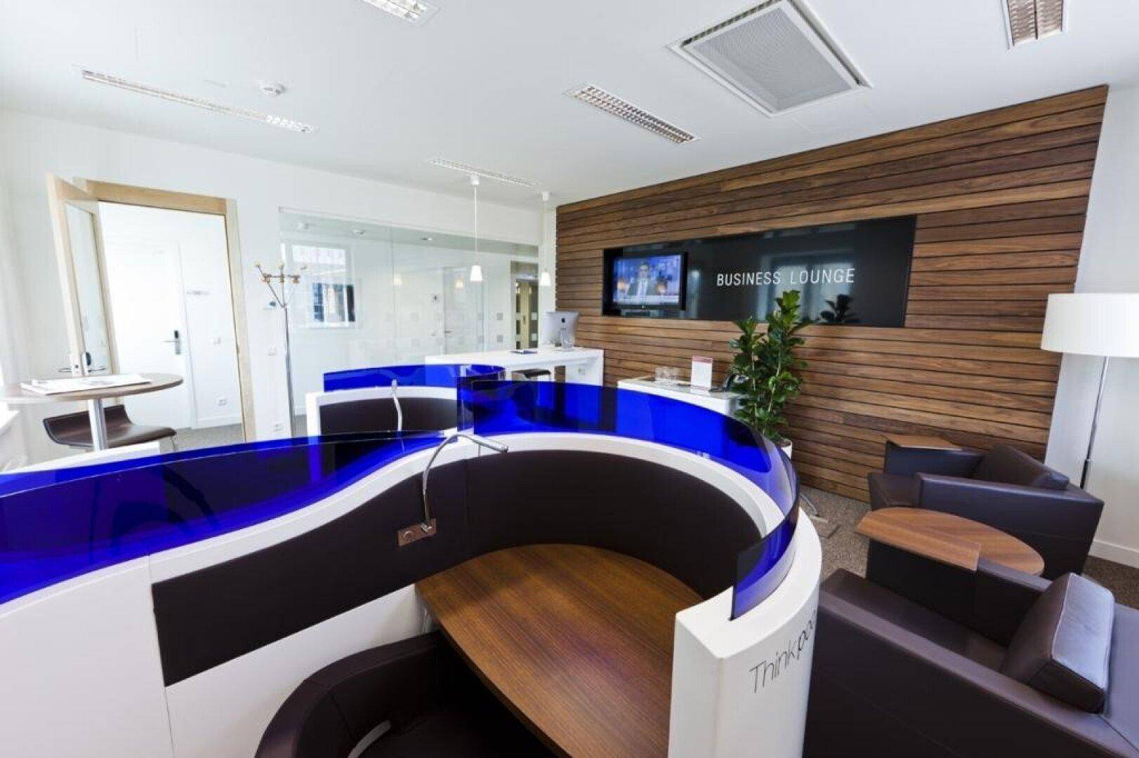 Moderne Business Lounge mit blauen Designelementen, Holzvertäfelung und bequemen Sesseln.