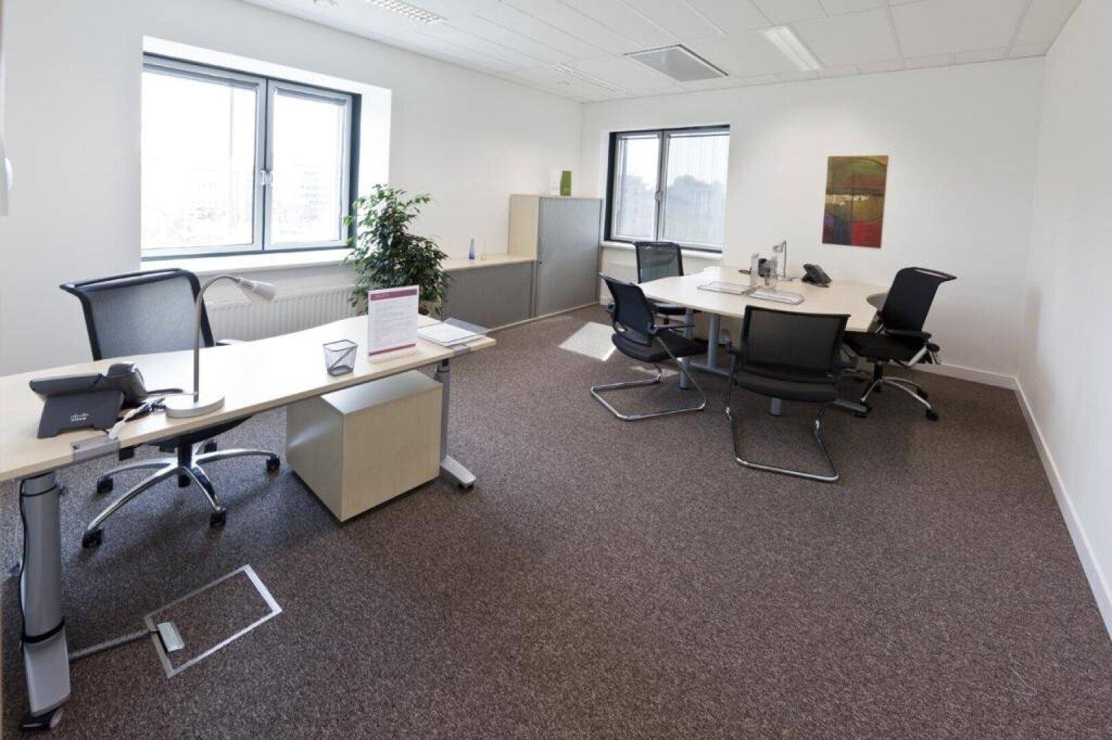 Offener Bürobereich mit mehreren Arbeitsplätzen, Schreibtischen und Bürostühlen am Fenster.