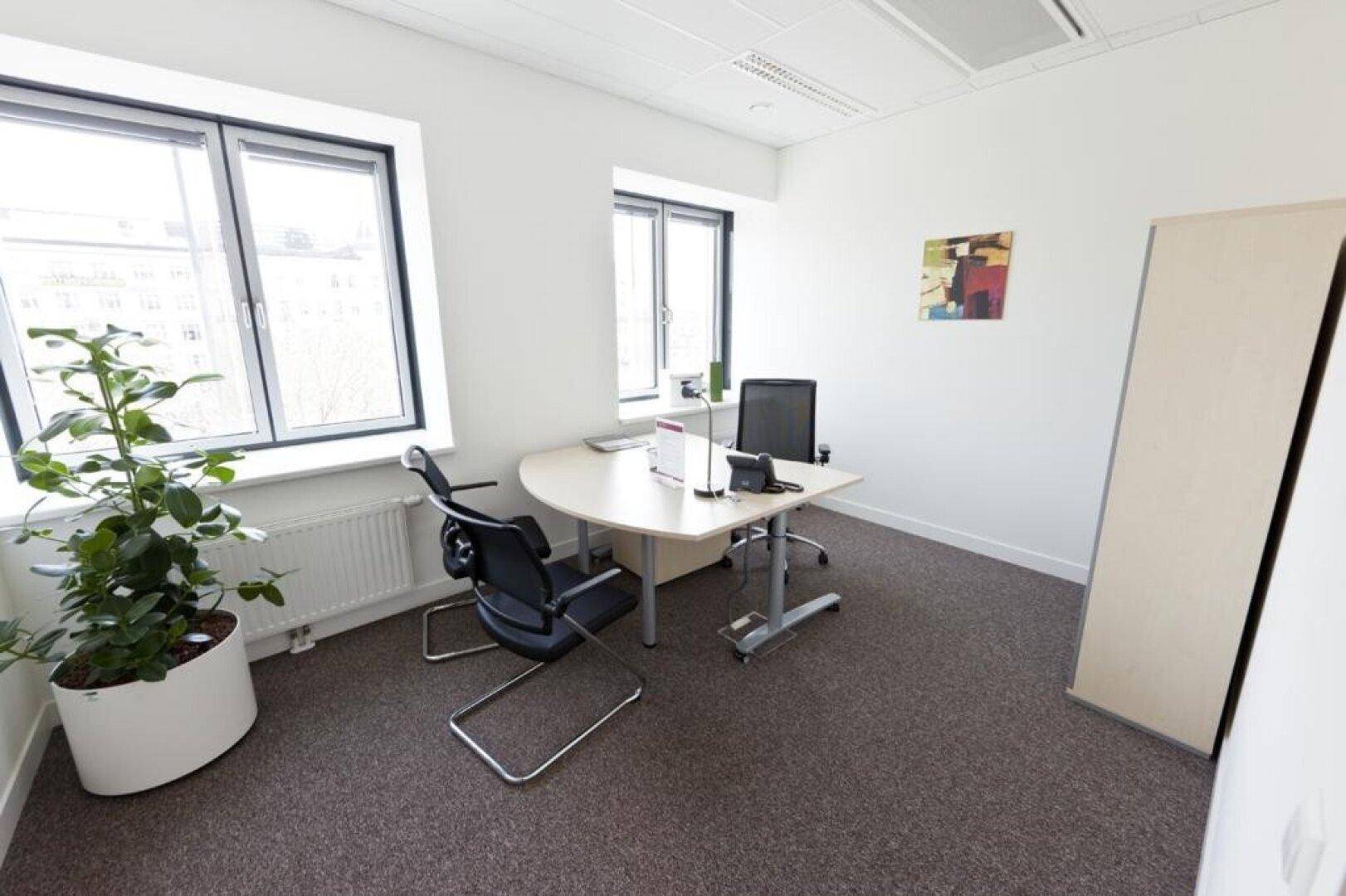 Einzelbüro mit Schreibtisch, Bürostuhl, Teppichboden und großen Fenstern für viel Tageslicht.