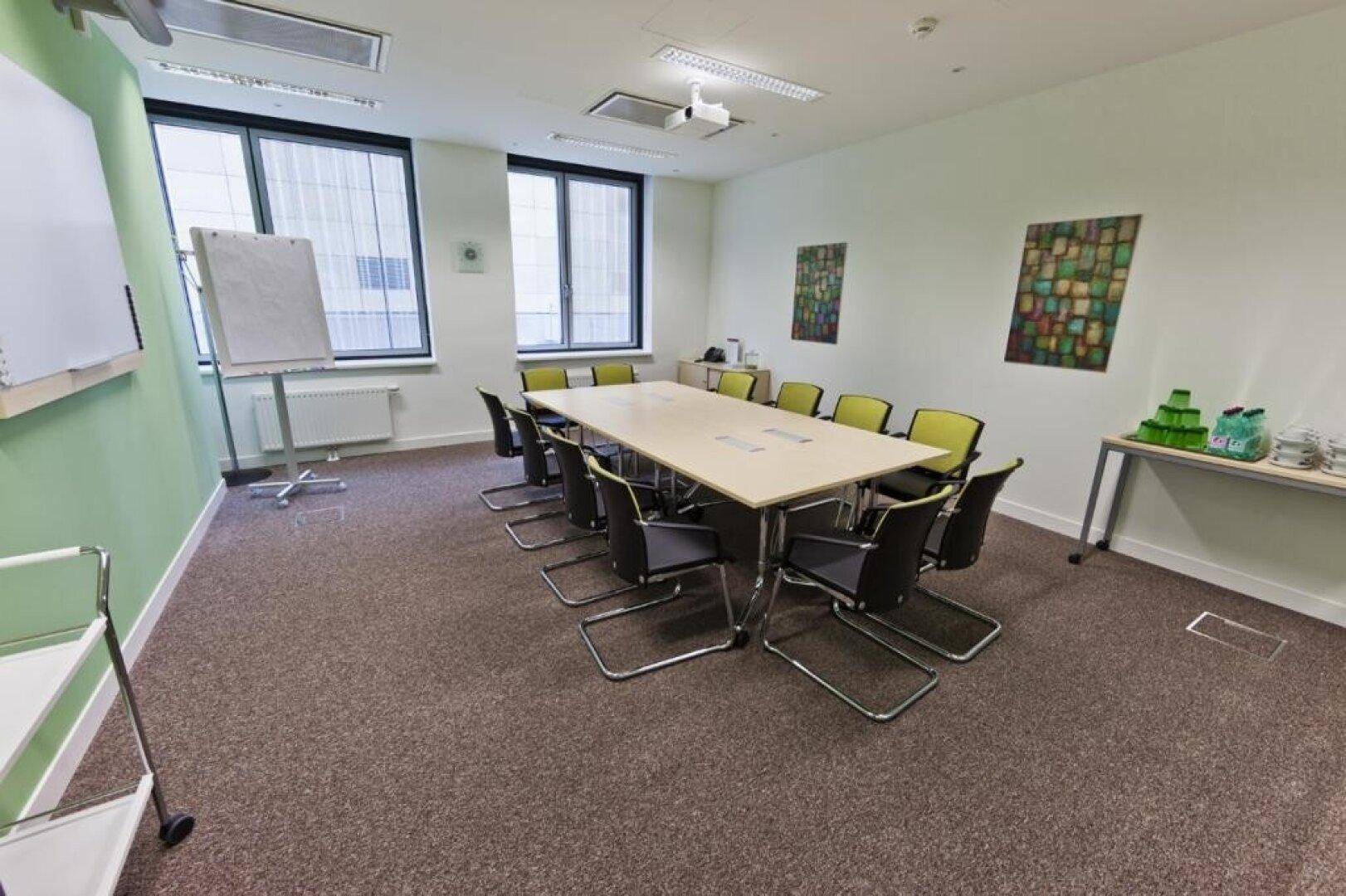 Geräumiger Konferenzraum mit großem Tisch, vielen Stühlen und einem Projektor an der Decke.