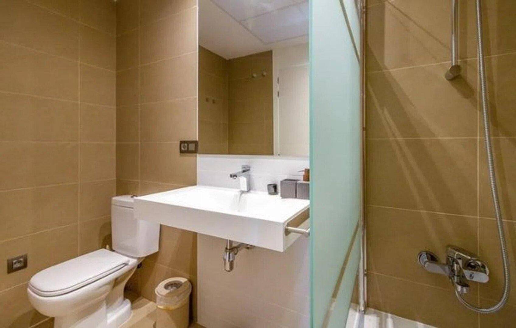 Modernes Badezimmer mit beigefarbenen Fliesen, schwebendem Waschbecken und Duschbereich.