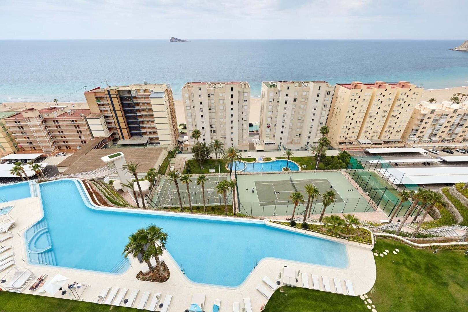 Luftaufnahme einer Wohnanlage mit großem Pool, Tennisplatz und Meerblick.