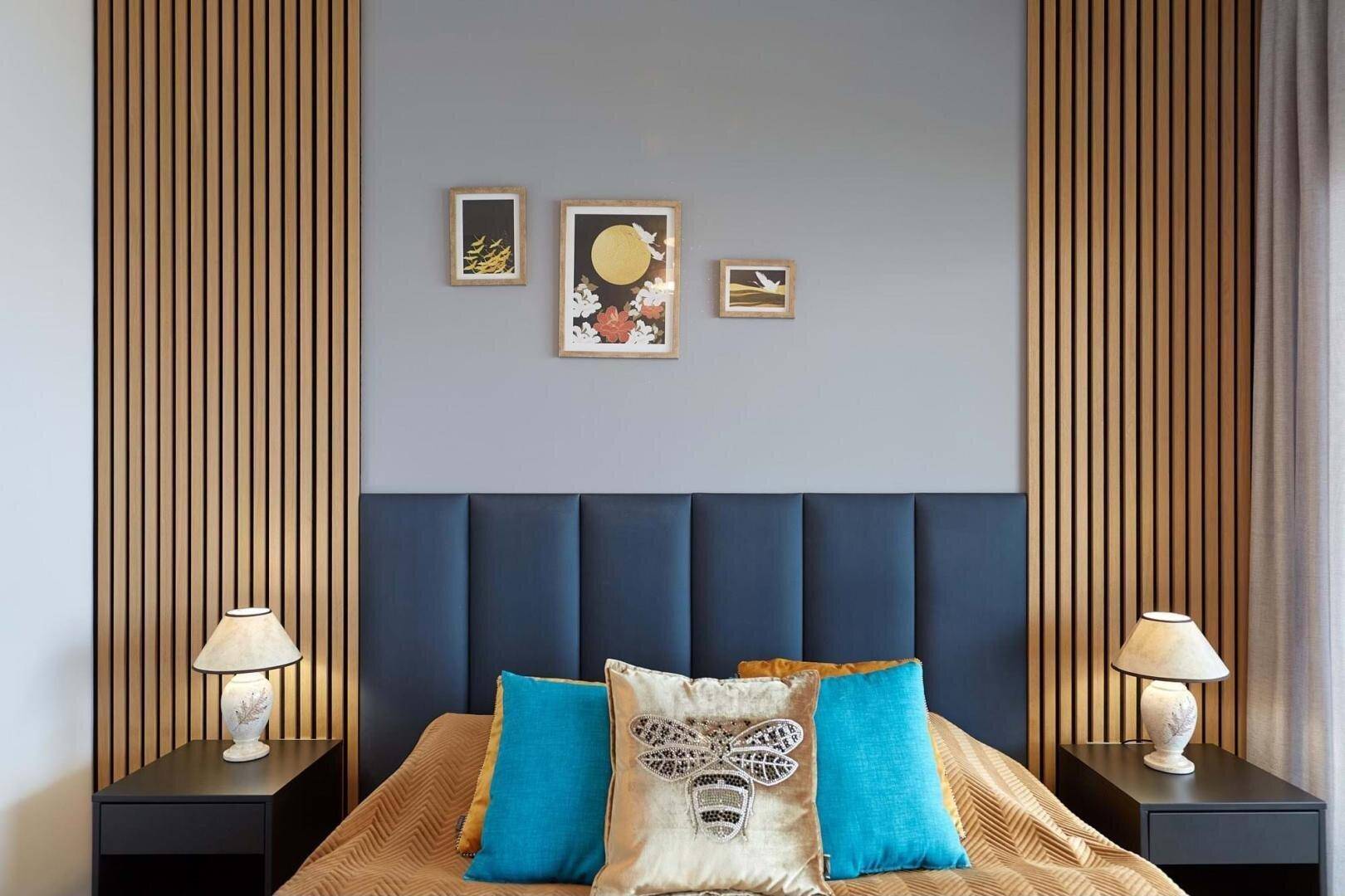Modernes Schlafzimmer mit gepolstertem Kopfteil, Holzlamellen und Nachttischen.