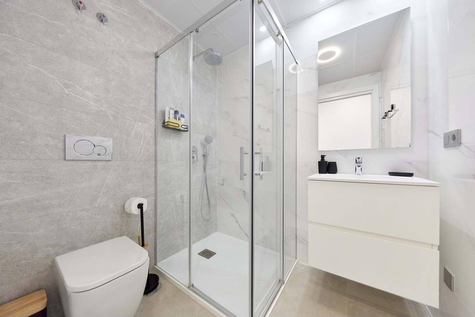Helles Badezimmer mit moderner Duschkabine, Einzelwaschbecken und Wand-WC.