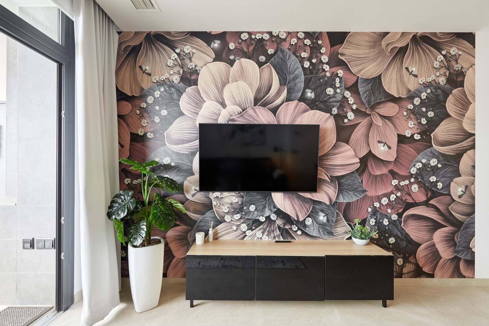 Wohnzimmer mit großer Blumentapete, Fernseher und Zugang zu einem Außenbereich.