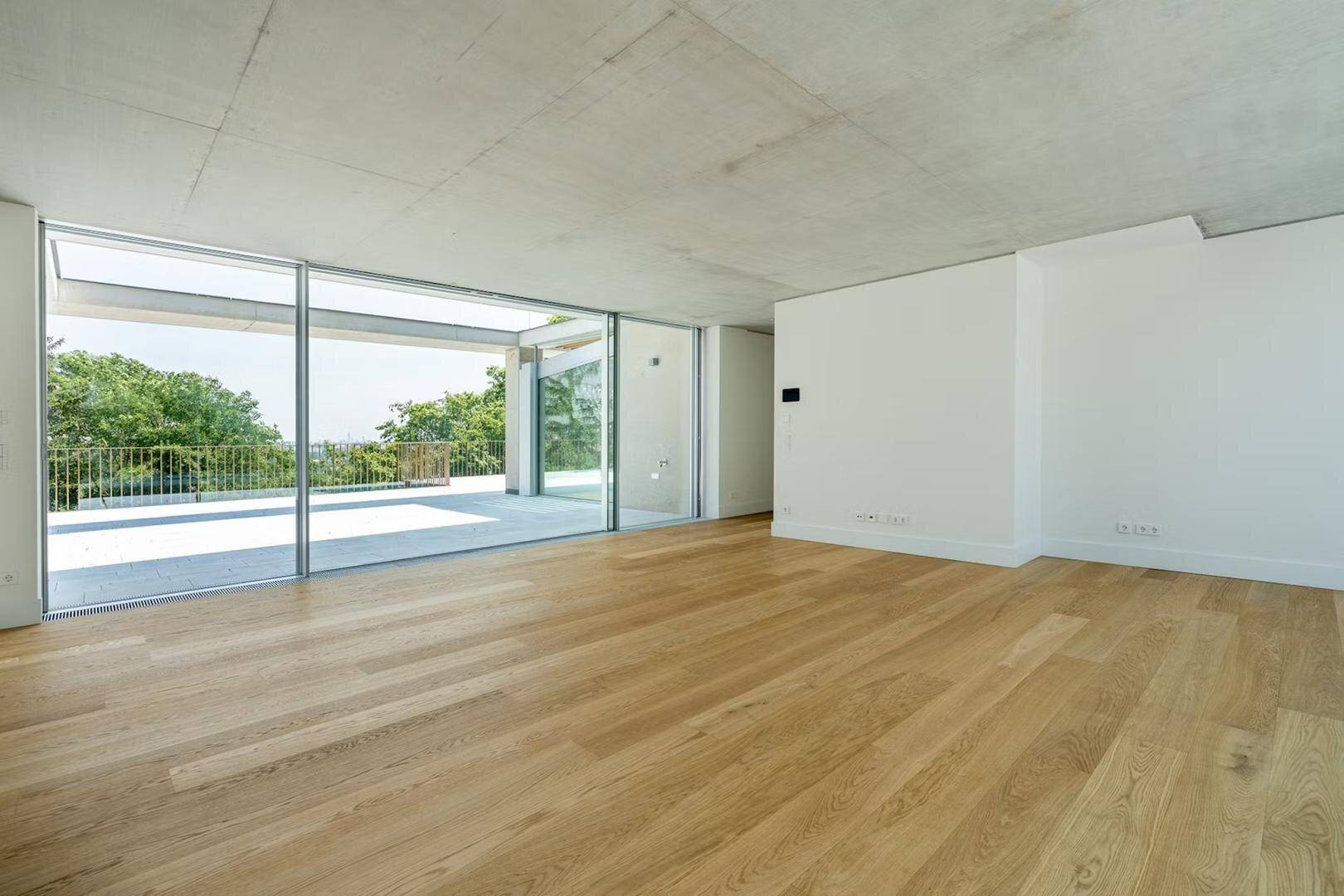 Geräumiges, unmöbliertes Wohnzimmer mit Holzboden und bodentiefen Fenstern zur Terrasse.