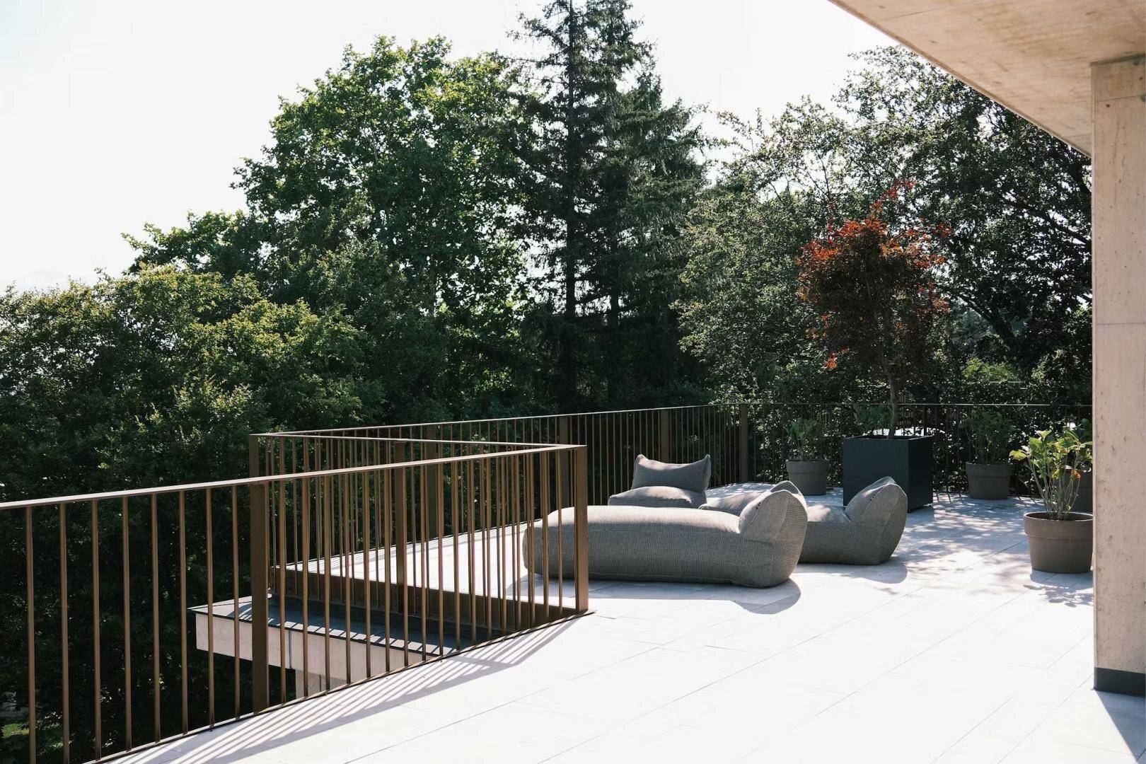 Sonniger Außenbereich mit Loungemöbeln und Blick auf die umliegende Baumlandschaft.