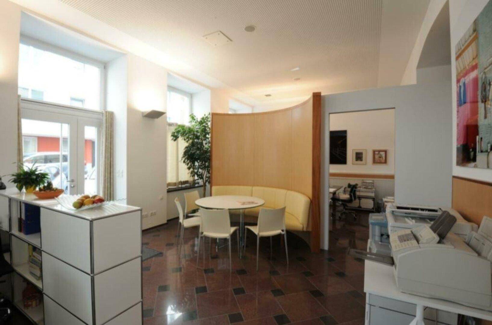 Offener Bürobereich mit einer runden Sitzecke, Pflanzen und Zugang zu einem weiteren Raum.