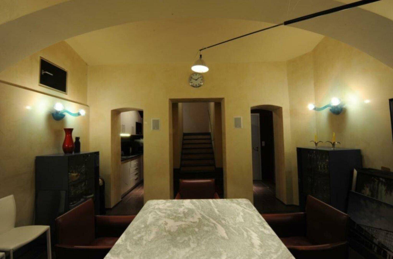 Gewölbter Raum mit einem Marmortisch, Ledersesseln und Blick auf eine Treppe.