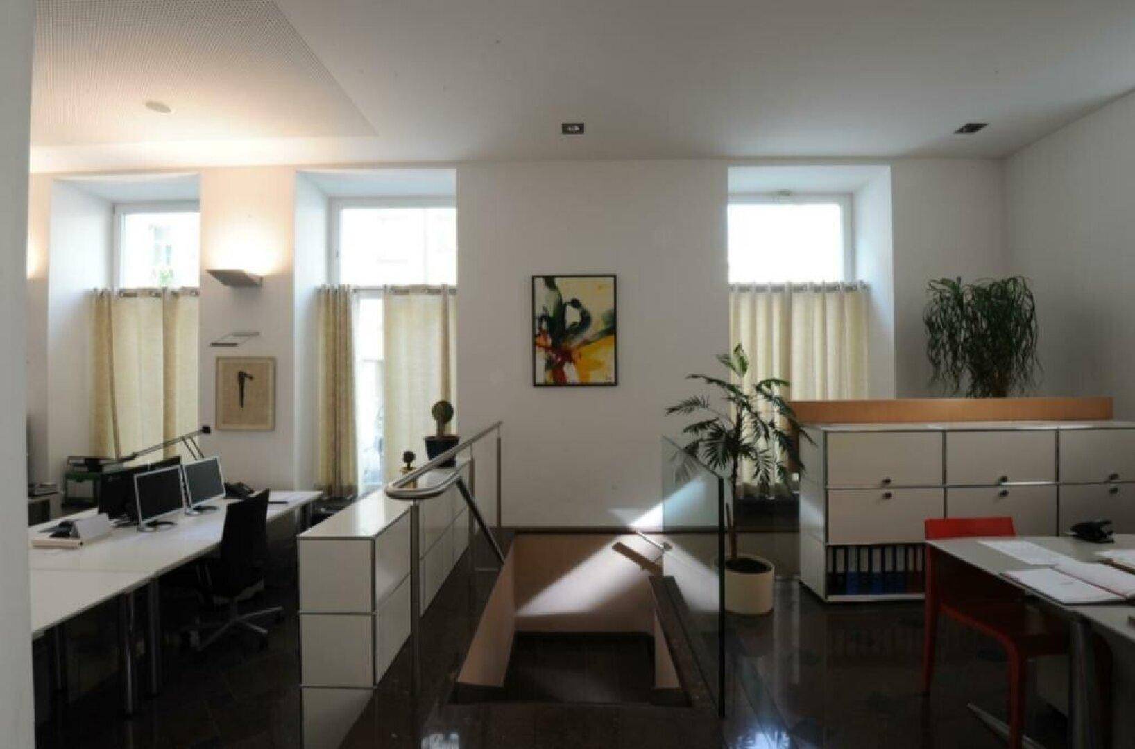 Büroraum mit zwei großen Fenstern, Pflanzen und einem Übergang mit kleiner Rampe.