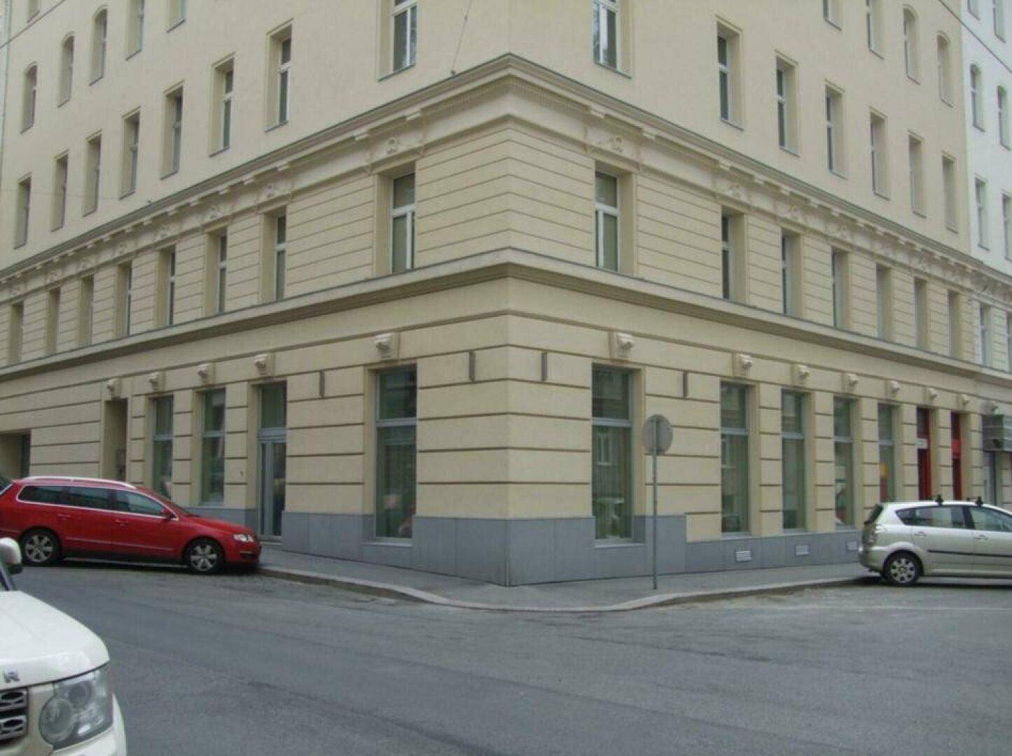 Eckgebäude mit klassischer Fassade, vielen Fenstern und parkenden Autos auf der Straße.