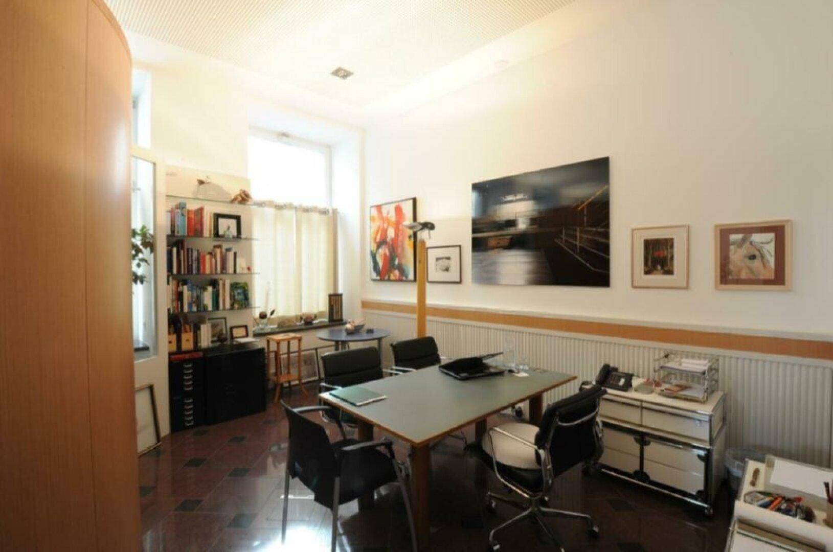 Besprechungsraum mit einem großen Tisch, Büchern und Kunstwerken an den Wänden.