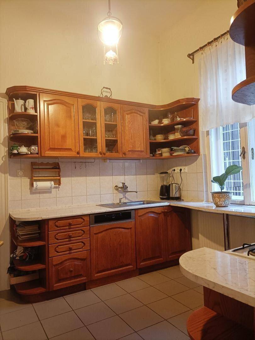 Klassische Holzküche mit Einbauschränken, Fliesenboden und einem Fenster mit Vorhang.