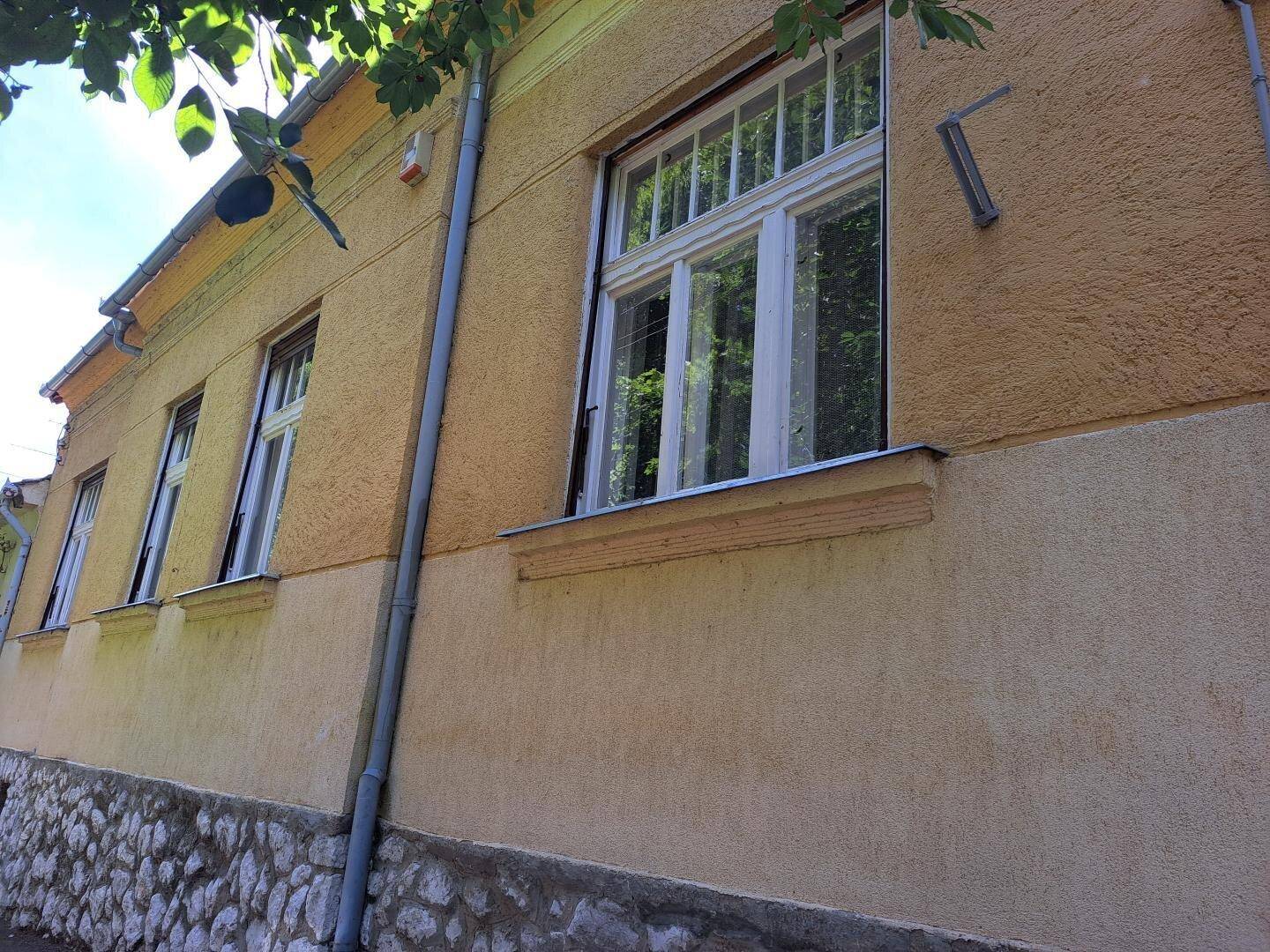 Detailansicht der gelben Hausfassade mit weißen Fenstern und einer steinernen Sockelverkleidung.