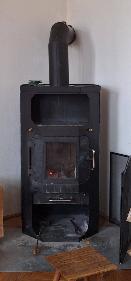 Freistehender Holzofen mit sichtbarem Feuer in einer Ecke des Raumes.