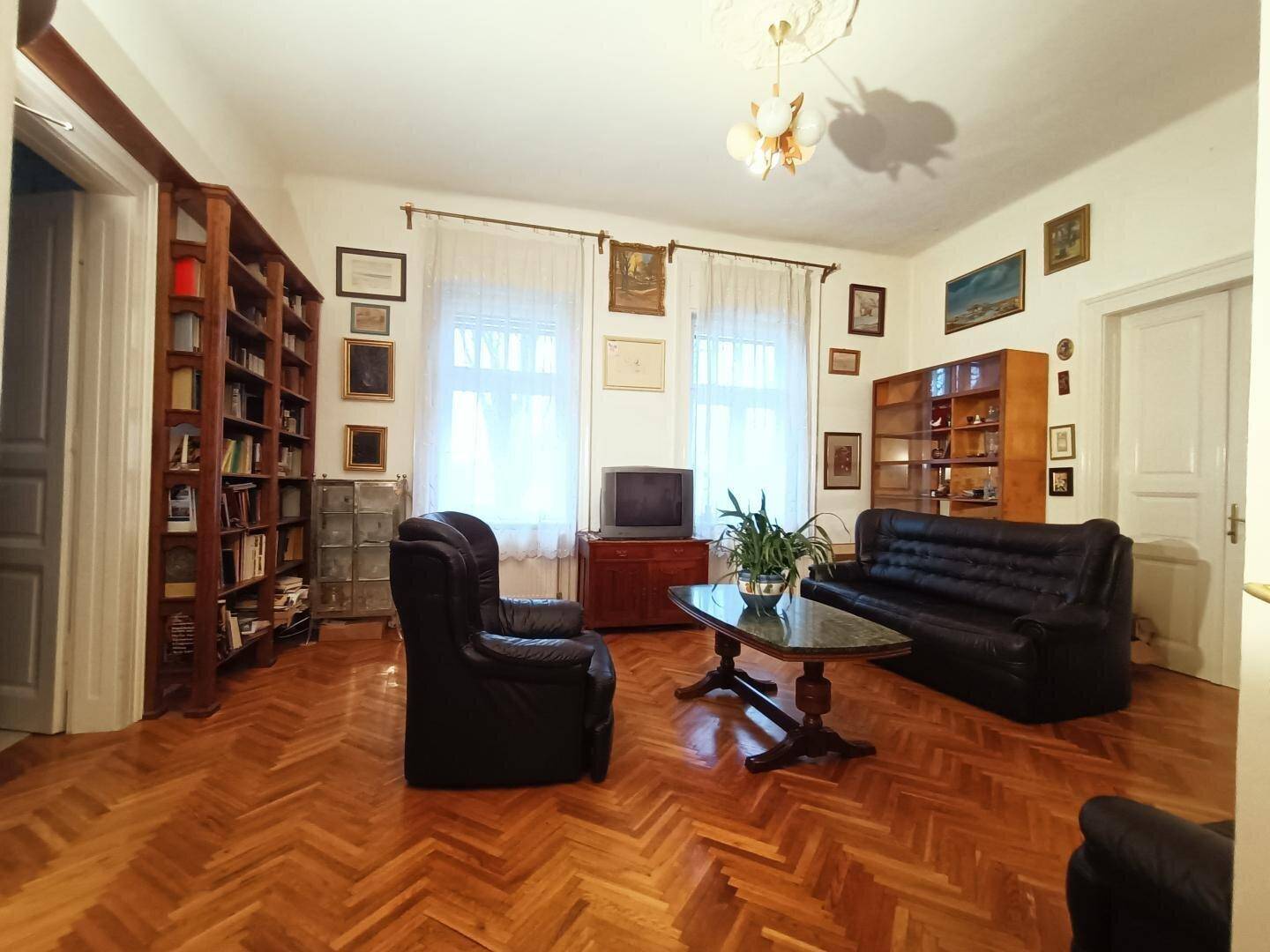 Geräumiges Wohnzimmer mit Ledermöbeln, Parkettboden, Bücherregalen und dekorativen Elementen.