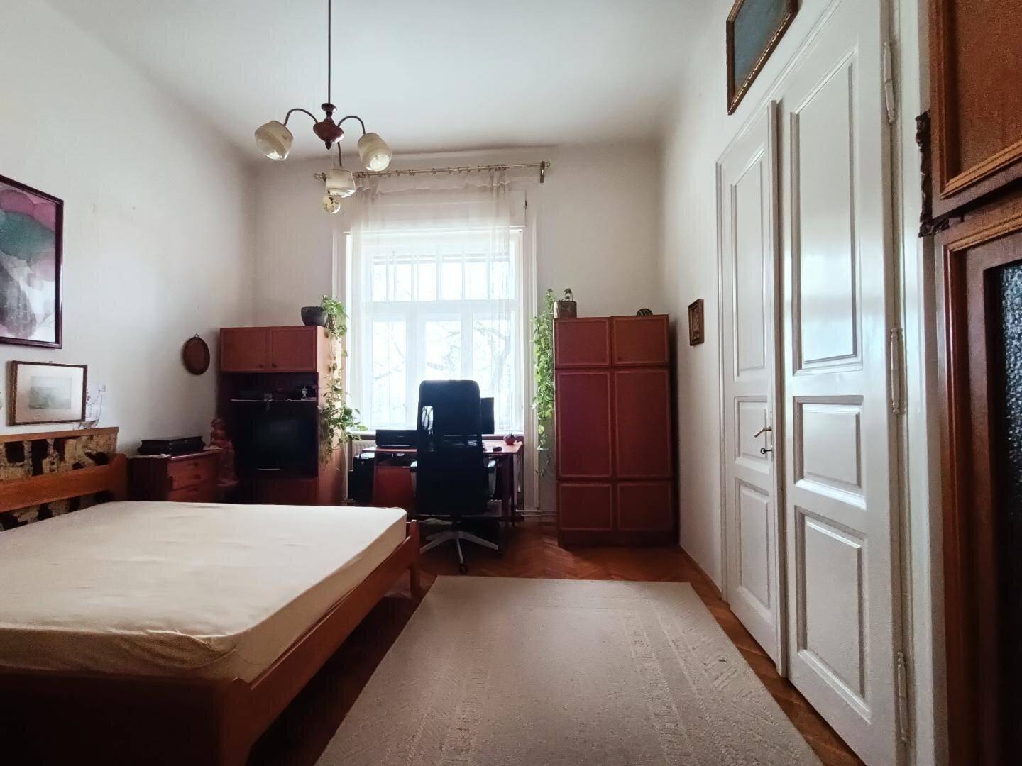 Schlafzimmer mit Holzbett, Schränken, Parkettboden und einem Fenster mit hellem Vorhang.