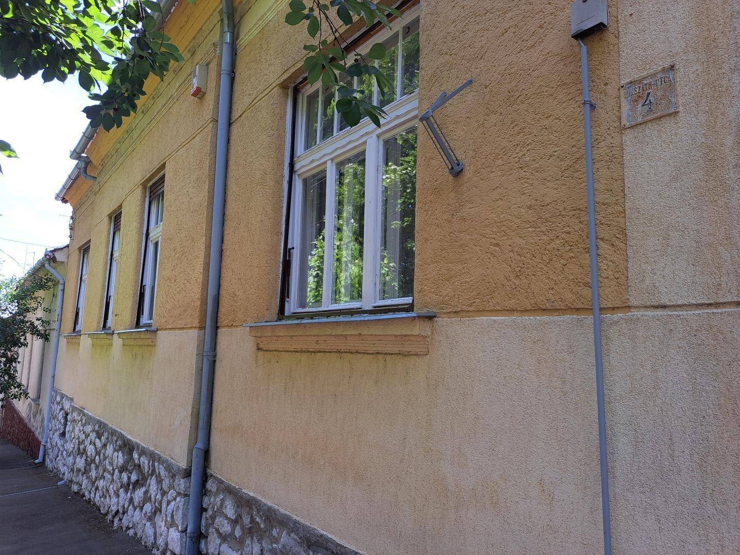 Gelbe Hausfassade mit weißen Fenstern, steinernem Sockel und sichtbarer Hausnummer 4.