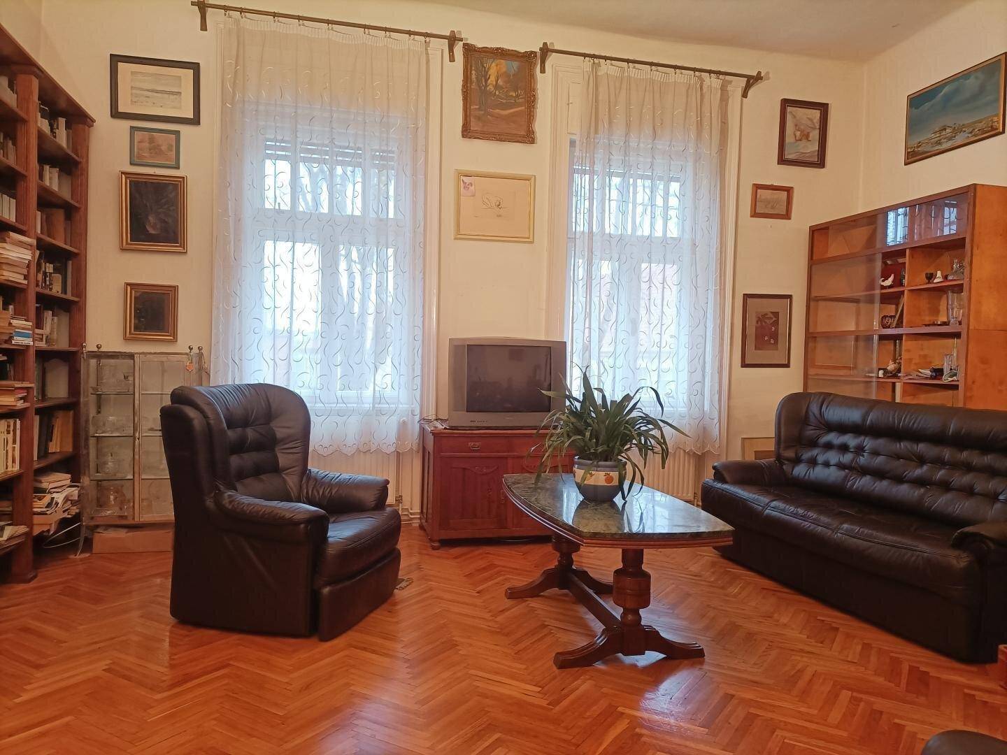 Gemütliches Wohnzimmer mit Ledersofas, Holzboden, Bücherregalen und großen Fenstern.