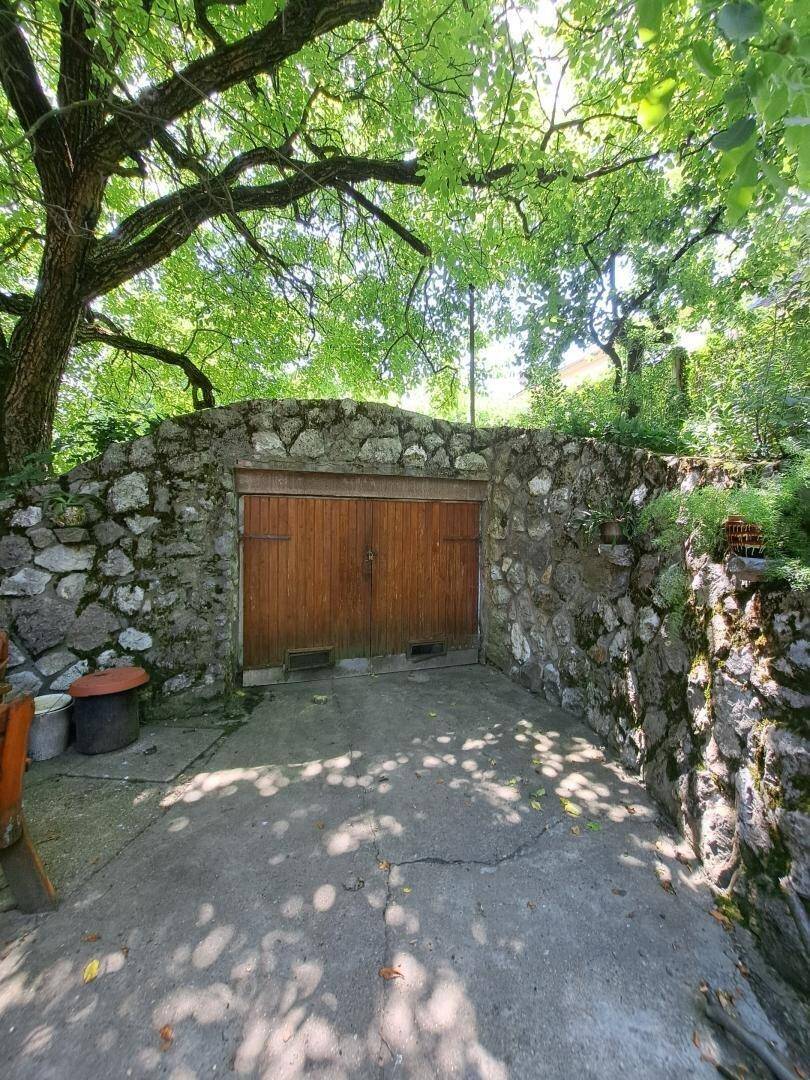 Rustikale Steinmauer mit einem großen Holztor, das den Eingang zu einem Grundstück markiert.