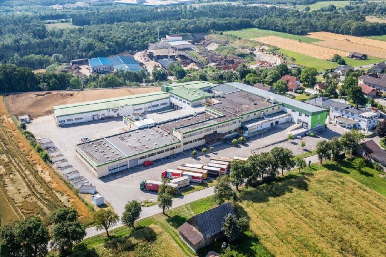 Luftaufnahme eines weitläufigen Industrie- und Gewerbekomplexes mit umliegenden Feldern und Wäldern.