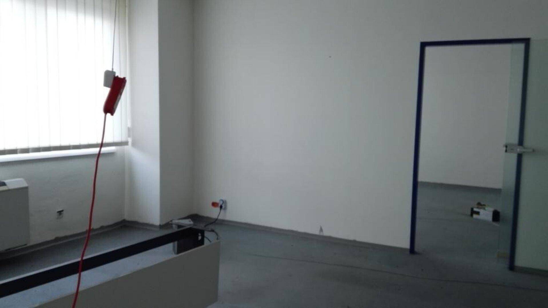 Leeres Büro mit grauem Boden, weißen Wänden und einem blauen Türrahmen, mit einem roten Verlängerungskabel.