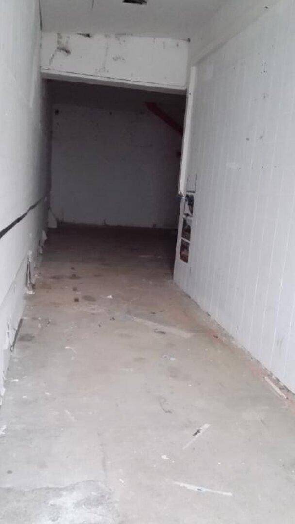 Schmaler, unfertiger Flur oder Lagerbereich mit Betonboden und weiß gefliesten Wänden.